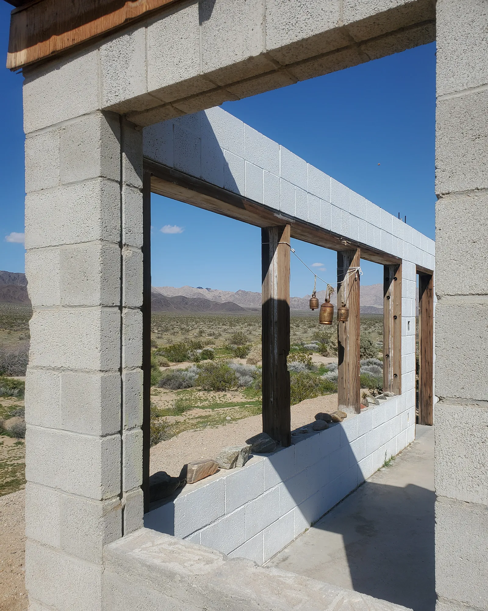 Desert landscape viewed through an unfinished stone doorway with ceremonial bells, representing the space between lives.